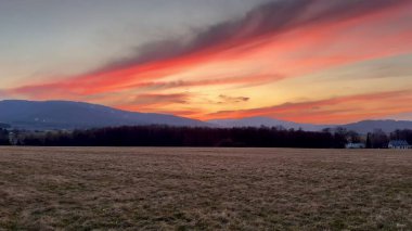 Nefes kesen bir gün batımı dingin bir manzaranın üzerindeki canlı renklerle genişleyen gökyüzünü canlı bir şekilde aydınlatıyor.