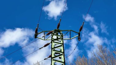 Pofuduk beyaz bulutlu açık mavi gökyüzüne karşı etkileyici bir elektrik iletim kulesi.
