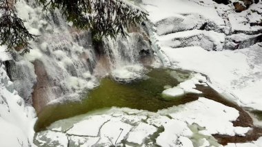 Parlak kar ve buzla çevrili güzel çağlayan bir şelalenin yer aldığı pitoresk bir kış sahnesi hayal edin.