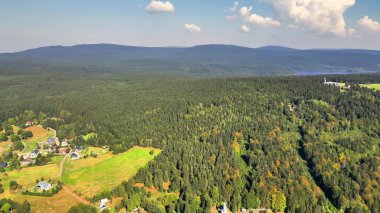 Uçsuz bucaksız ormanları ve dingin manzaraları gösteren bir hava manzarası berrak mavi bir gökyüzünün altında güzelce gerilmiş.