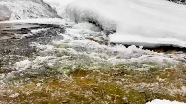 Eriyen karın altında akan temiz bir derenin resimsel bir görüntüsü, kış güzelliğini gözler önüne seriyor.