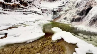 Karlı bir ormanda fırtınalı donmuş bir şelale..