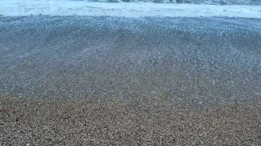 Sakin okyanus dalgaları, alacakaranlıkta pürüzsüz bir çakıl taşının üzerinde süzülüp huzurlu ve huzurlu bir atmosfer yaratıyor.