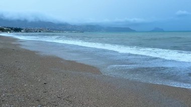 Resimli ve sakin bir sahil sahnesi bulutlu bir günde yumuşak dalgaların kumlu kıyıya hafifçe vurduğu.