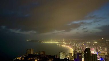 Göz kamaştırıcı bir şehir manzarası. Gökyüzü bulutlu ve gece ışıl ışıl parlıyor.