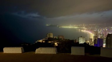 Karamsar gökyüzünün altında parıldayan kıyı şeridi boyunca şehrin ışıklarını gösteren nefes kesici bir panorama.