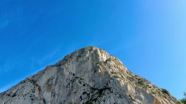 Görkemli bir dağ zirvesi berrak mavi bir gökyüzüne karşı yükseliyor, nefes kesici güzellikler ve ihtişam sergiliyor.