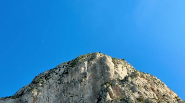 Engebeli, kayalık bir dağın nefes kesici manzarası görkemli, parlak, mavi gökyüzüne karşı duruyor.