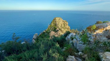 Nefes kesici bir kıyı manzarası dingin ve dingin okyanusa karşı kurulu kayalık kayalıkları canlı bir şekilde gösteriyor.