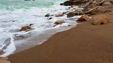 Sersemletici ve sakin bir plaj sahnesi yumuşak, yumuşak dalgaların ritmik bir şekilde kayalık kıyılara vuruşunu güzel bir şekilde gösteriyor.