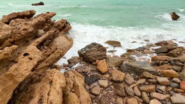 Kıyıya çarpan kayalık oluşumların ve canlı turkuaz dalgaların olduğu güzel bir sahil manzarası..