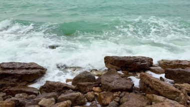 Sakin bir sahil şeridi boyunca kayalık oluşumlara çarpan dalgaların nefes kesici güzelliğini hissedin.