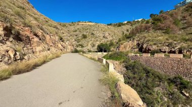 Göz kamaştırıcı güzellikte bir patika kayalık arazide, berrak mavi gökyüzünün altında yemyeşil bir yer kaplar.