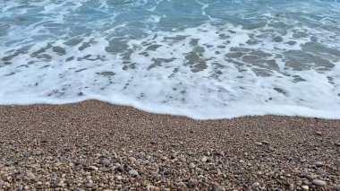 Yumuşak dalgalar hoş, çakıllı bir plaja hafifçe çarpıyor, güzel ve sakin bir sahil atmosferi yaratıyor.