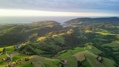 Bu hava manzarası canlı, renkli bir gökyüzünün altında yemyeşil tepeler ve görkemli dağları barındırır.