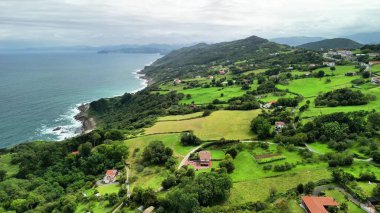 Sergilenen göz kamaştırıcı ve nefes kesici hava manzarası dingin ve güzel bir sahil şeridi boyunca yemyeşil tepeler.