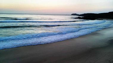 Gün batımında çekilen güzel ve sakin bir sahil sahnesi huzurlu bir sahil şeridi boyunca hafif dalgalar sergiliyor.
