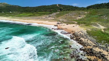 Huzurlu bir kıyı manzarasında berrak turkuaz dalgaların yer aldığı şaşırtıcı derecede güzel kumlu bir sahil.