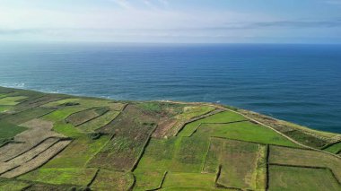 Titrek yeşil tarlaların nefes kesici ve çarpıcı hava manzarasını, dingin bir okyanus manzarasının yanında tecrübe edin.