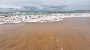 Nazik dalgaların güzel sakin manzarası bulutlu gökyüzünün altındaki altın kumlu kumsalda durmadan süzülüyor.