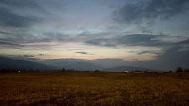 Anımsatıcı ve pitoresk bir alacakaranlık sahnesi geniş kırsal bir alanda yavaşça yuvarlanan tepeleri gösteriyor.
