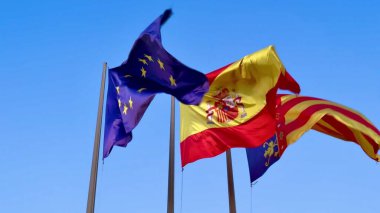 Avrupa Birliği ve İspanyol ulusal bayrakları parlak mavi gökyüzünün altında gururla sallanıyor.