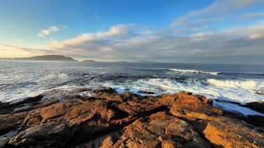 Nefes kesici bir manzara dalgaları sergiliyor dalgalar engebeli kayalara çarpıyor deniz kenarında canlı bir gündoğumu sırasında