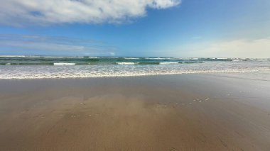 Huzurlu ve huzurlu bir sahil manzarası. Yumuşak, rahatlatıcı dalgalar, berrak mavi gökyüzünün altında.