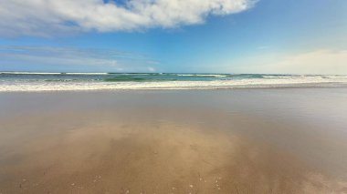 Nefes kesen bir plaj sahnesi, hafif dalgaları tasvir eder canlı, berrak bir mavi gökyüzüne karşı.