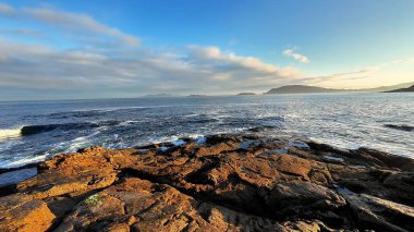 Engin okyanusla canlı bir gökyüzünün altında zarif bir şekilde buluşan kayalık kıyı şeridinin nefes kesici bir görüntüsü.