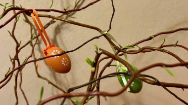 Şenlikli turuncu ve yeşil Paskalya yumurtaları yaratıcı bir şekilde dallara asılır ve hoş dekoratif parçalar olarak servis edilir.