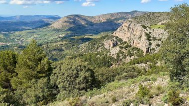 Nefes kesici manzara kayalık tepeleri, yemyeşil vadilerin yanında sergiliyor, hepsi yukarıdaki parlak mavi gökyüzünün altında.
