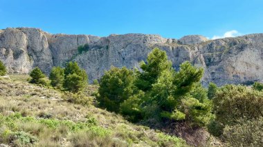 Göz kamaştırıcı bir dağ silsilesine, canlı yeşilliğe ve yukarıda açık mavi gökyüzüne sahip güzel bir manzara.