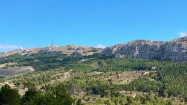 Nefes kesen panoramik manzara, canlı mavi gökyüzünün altındaki yemyeşil yemyeşil, çarpıcı dağlık araziyi gösteriyor.
