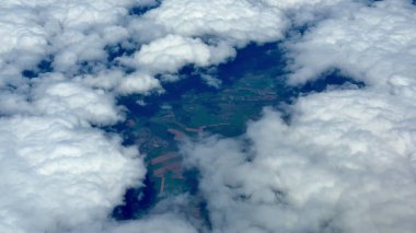Yumuşak, tüylü beyaz bulutlar tarafından kısmen gizlenmiş uçsuz bucaksız ve yemyeşil bir arazinin nefes kesici hava manzarası.