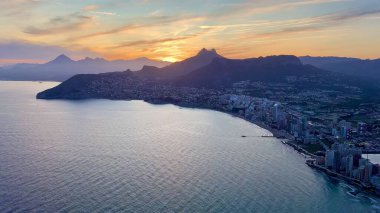 Çarpıcı ve resimli bir gün batımı görkemli dağlara karşı canlı kıyı şehrini güzel aydınlatıyor.