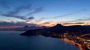 Göz kamaştırıcı bir günbatımı, kıyı şehrine canlı bir ışık saçar. Güzel ışıkları ve görkemli dağları aydınlatır.