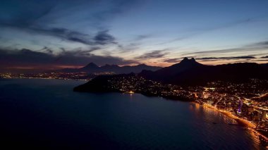 Parlak bir kıyı şehrinin göz kamaştırıcı hava manzarası. Gece aydınlandı, görkemli dağlarla çevrili.