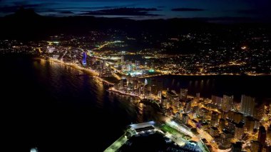 Geceleri kıyı şehrinin canlı ve renkli ışıklarını yansıtan kesinlikle nefes kesici bir hava manzarası.