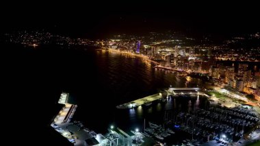 Gece ufkunun çarpıcı hava manzarası canlı şehir ışıklarını vurguluyor sahili güzel aydınlatıyor.