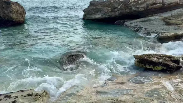 Huzurlu bir sahil sahnesi güzel bir şekilde dalgaların ritmik bir şekilde kayalara çarptığını gösteriyor.