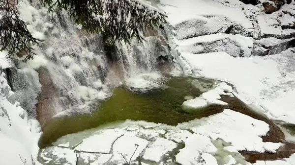 Parlak kar ve buzla çevrili güzel çağlayan bir şelalenin yer aldığı pitoresk bir kış sahnesi hayal edin.