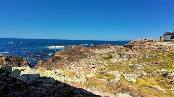 Berrak bir gökyüzünün altında parıldayan mavi okyanusun yanında engebeli, pürüzlü kayaları barındıran nefes kesici bir kıyı manzarası.