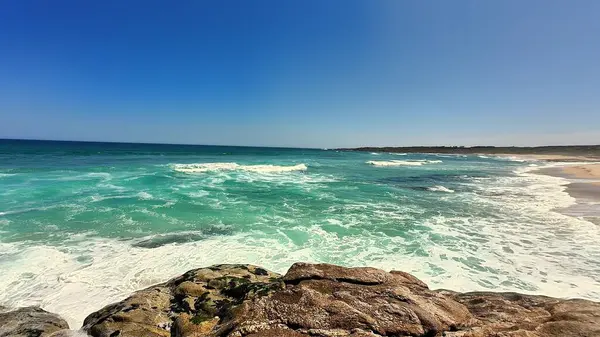 Göz kamaştırıcı bir sahil sahnesi canlı turkuaz sular ve güzel bir günde ışıldayan güneş ışığı kayaları sergiliyor.
