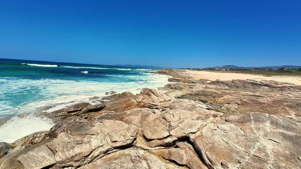 Engebeli kayalık sahilin şaşırtıcı güzellikteki manzarasında berrak mavi gökyüzü ve okyanus dalgaları çarpışıyor.
