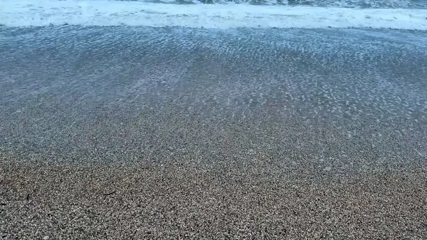 Sakin okyanus dalgaları, alacakaranlıkta pürüzsüz bir çakıl taşının üzerinde süzülüp huzurlu ve huzurlu bir atmosfer yaratıyor.