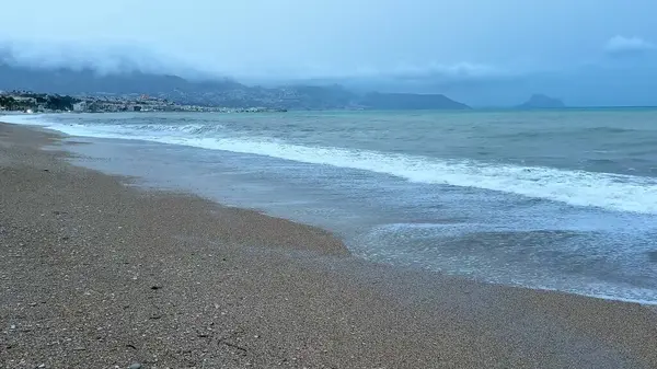 Resimli ve sakin bir sahil sahnesi bulutlu bir günde yumuşak dalgaların kumlu kıyıya hafifçe vurduğu.