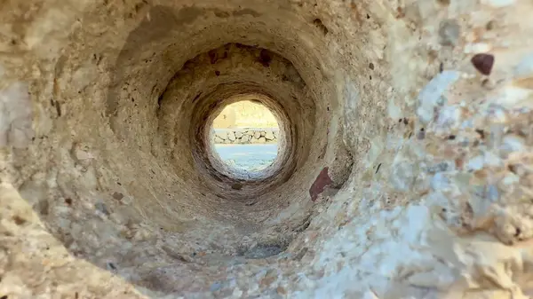 Dairesel bir kaya tüneli tarafından çerçevelenmiş büyüleyici ve nefes kesici bir manzara var, nefes kesici doğal bir manzara sergiliyor.