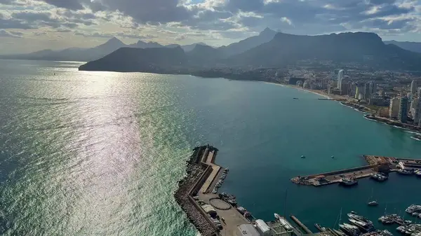 Sersemletici hava manzarası kıyı şehrini, dağları ve bulutlu gökyüzünün altında canlı marinayı gösteriyor..