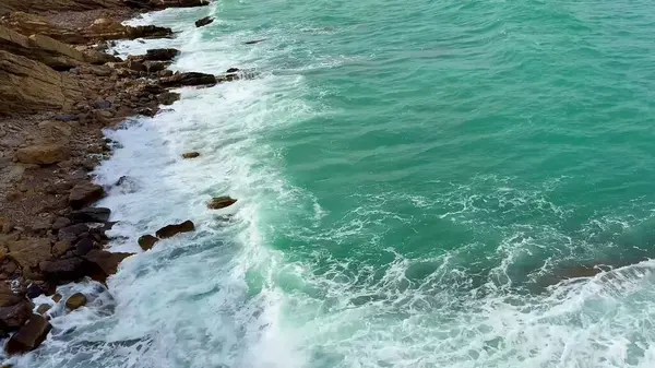 Bu hava manzarası, kayalık kıyı şeridi ve nazik dalgalarla karşılaşan çarpıcı turkuaz suları yakalar.